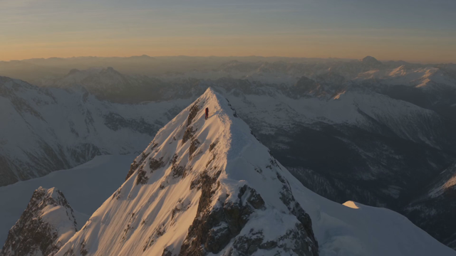 A climber reaches a snowy summit, pulls off her goggles and whispers 'We actually made it', wind gusts, rope clinking on the harness, breath visible in cold air