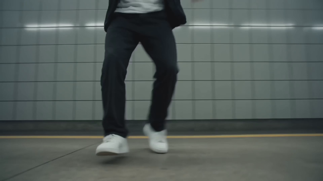 A breakdancer spins into a one-handed freeze on a subway platform, jacket flaring with the rotation, fluorescent light flicker, sneakers squeaking on concrete, beat echoing off the tiles