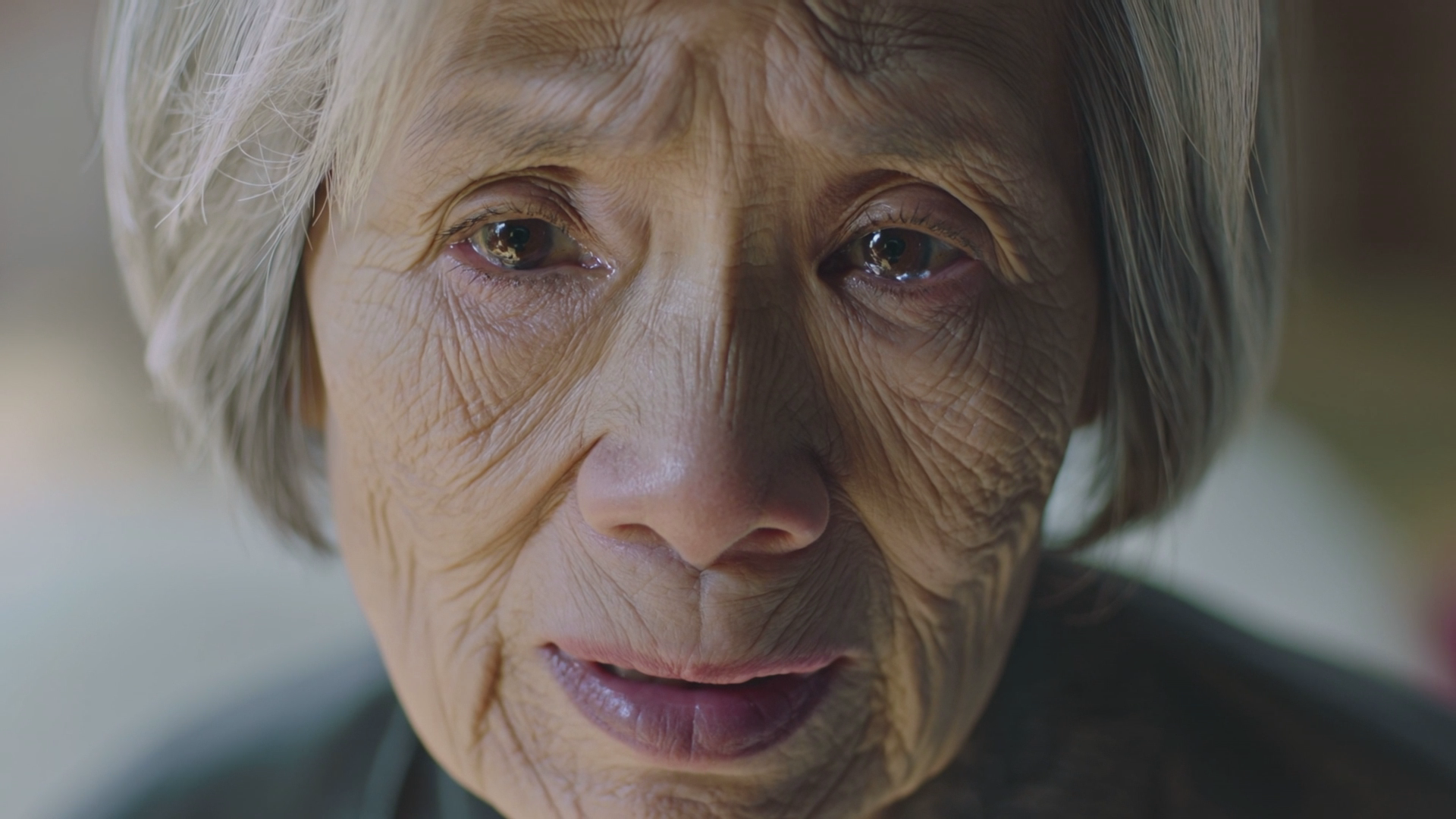 Close-up portrait of an elderly Asian woman, soft window light, shallow depth of field. A tear rolls down her cheek as she says 'I still remember the day we met... like it was yesterday.' Cinematic 35mm film look, emotionally powerful.