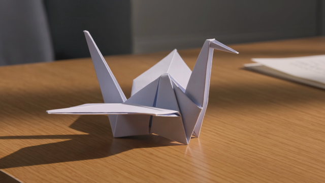 A paper origami crane on a desk slowly unfolds, reshapes itself, and takes flight through an open window into a paper-craft world, whimsical multi-shot sequence