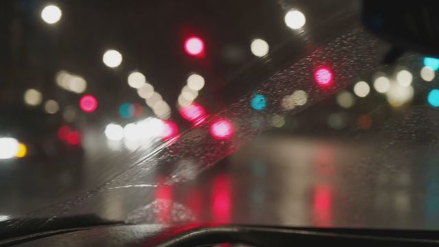A taxi driver glances in the rearview mirror at night and says 'First time in the city?', rain on the windshield, wipers keeping rhythm, distant sirens