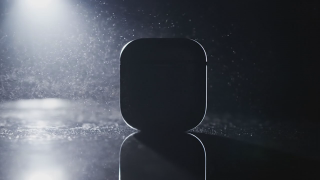Studio product hero shot of [a matte black wireless earbud case] rotating slowly on a glossy dark surface, dramatic rim lighting, dust particles in the light beam, deep bass pulse